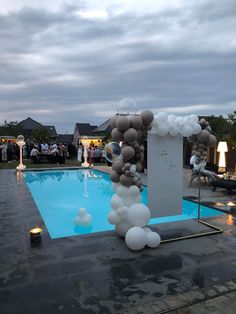 an outdoor pool decorated with balloons and streamers for a wedding reception in the evening