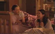 two women laughing while laying in bed together