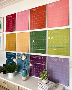 a wall with calendars on it and some plants in vases next to each other