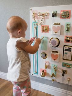 a baby standing in front of a bulletin board with lots of magnets on it