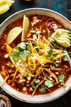 a white bowl filled with chili, cheese and avocado on top of a table