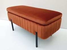 an orange velvet bench with black legs on a white floor in front of a wall