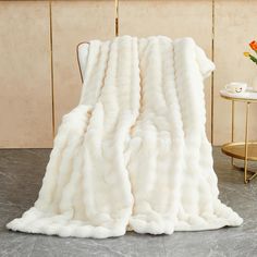 a white fur blanket sitting on top of a chair next to a vase with flowers