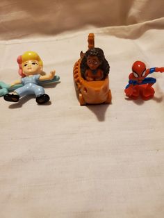 three toy figurines sitting next to each other on a white cloth covered surface