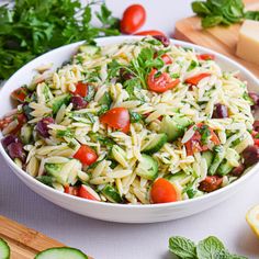 a white bowl filled with pasta salad next to sliced cucumbers and lemon slices