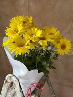 a bouquet of yellow flowers sitting on top of a wooden stand next to a wall