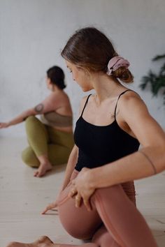 two women are sitting on the floor in yoga gear and one is holding her leg up