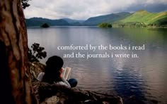 a woman sitting on top of a rock next to a lake with a book in her hand