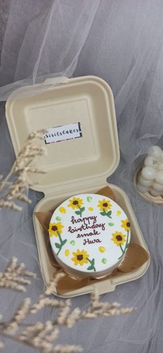 a birthday cake in a box with flowers on the side and some marshmallows