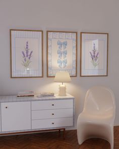 a white chair sitting next to a table with a lamp on top of it in front of two framed pictures