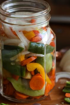 a glass jar filled with sliced vegetables on top of a wooden table