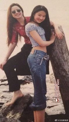 two young women standing next to each other on top of a wooden post near the ocean