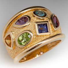 This wide band ring features six (6) colored gemstones, of varying cuts, that are set in high polished bezels across the face and accented by a recessed stippled texture. The ring measures 16.0mm at the top, rises 4.7mm above the finger, tapering to 6.3mm wide and 1.5mm thick at the base of the shank. The ring is currently a size 6.5. Colored Gemstones, Wide Band Ring, Wide Band Rings, Wide Bands, Bezel Setting, Gemstone Colors, Band Ring, Ring Designs, Band Rings