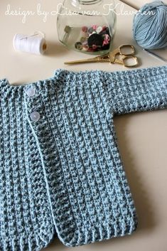 a blue knitted sweater sitting on top of a table next to scissors and yarn