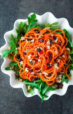 a white bowl filled with carrots, nuts and green leafy salad on top of a table