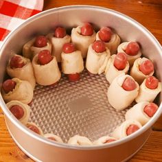 a metal pan filled with hot dogs on top of a wooden table next to a red and white checkered napkin