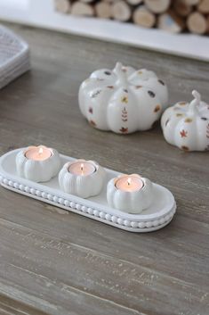 three white pumpkins sitting on top of a wooden table next to some lit candles