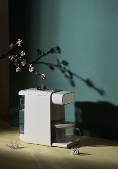 a white coffee maker sitting on top of a wooden table next to a vase with flowers