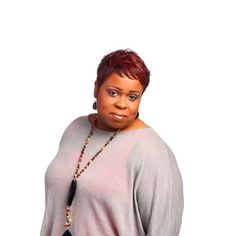 a woman with red hair wearing a gray top and black pants, standing in front of a white background