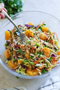 a person holding a fork in a bowl filled with salad