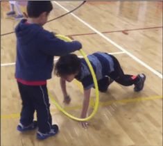 two young children playing with a hula hoop in an indoor gym, one boy is wearing blue and the other girl is black