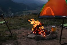 a campfire with a cup of coffee in front of it on top of a hill