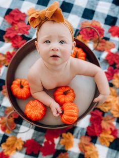 a baby sitting in a bowl with pumpkins