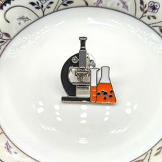 a white plate topped with a microscope and flasks filled with orange liquid on top of it