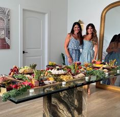 two women standing in front of a table full of food