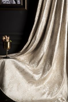 a gold vase sitting on top of a wooden table next to a white drapes