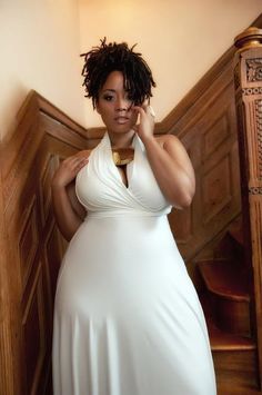 a woman in a white dress is talking on her cell phone while standing next to stairs