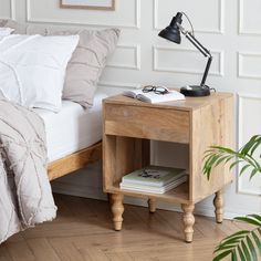 a bed with a wooden night stand next to a plant and a lamp on top of it