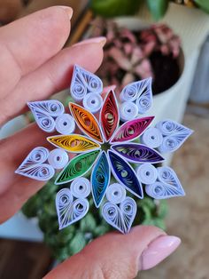 a hand holding an origami flower in front of a potted plant