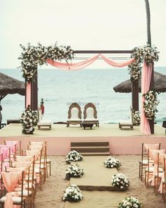 an outdoor ceremony set up on the beach with pink and white flowers in front of it