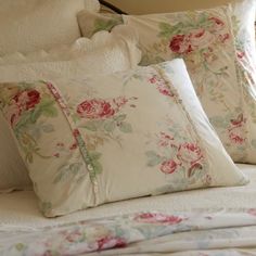 pillows and blankets on a bed in a bedroom with white linens, pink roses and green leaves