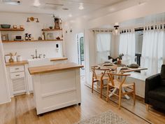 a kitchen and dining room with white walls, wood floors and open shelving on the wall