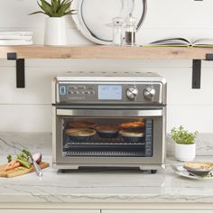 an oven with food cooking in it on top of a counter next to plates and utensils