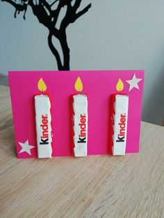 three candy bars with lit candles are on a pink card