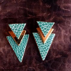 two green and gold triangle shaped earrings sitting on top of a brown cloth covered surface