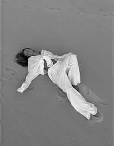 a woman laying on the beach in white clothes