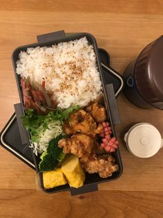 a plastic container filled with rice, meat and veggies next to a coffee cup