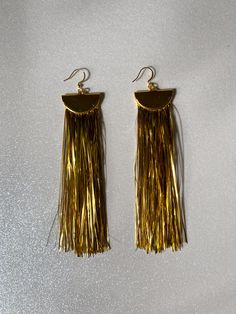 Gift yourself or a friend a unique set of gold metallic tinsel tassel earrings for a special occasion. They feature 18K gold and a tinsel fringe that dangle perfectly from your ears for a festive look. Upgrade any outfit for a holiday party, New Year’s Eve, or any special event! Materials: 18K gold hook, gold half moon, tinsel fringe Fringe Length: 4in Gold Dangle Tassel Earrings For Celebration, Party Tassel Earrings With Fringe, Gold Tassel Earrings For Party, Gold Elegant Tassel Earrings For Party, Gold Latkan Earrings For Party, Gold Tassel Drop Earrings For Gifts, Festive Gold Jewelry With Tassels, Gold Jewelry With Tassels For Celebrations, Gold Tassel Dangle Earrings