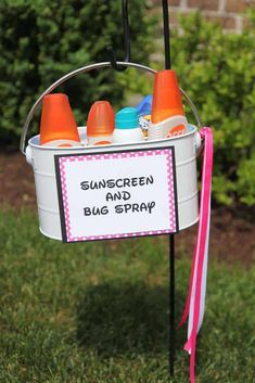 a bucket with sunscreen and bug sprays on it sitting in the grass next to some bushes