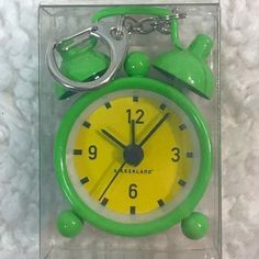 a green and yellow alarm clock with keychain on it's side in a clear box