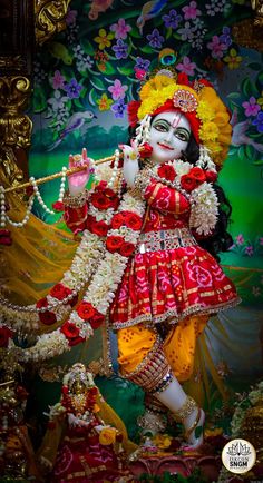 a statue of the hindu god in front of a colorful wall with flowers on it