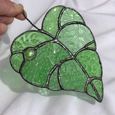 a hand holding a green leaf shaped glass decoration on a white sheet with a black bead