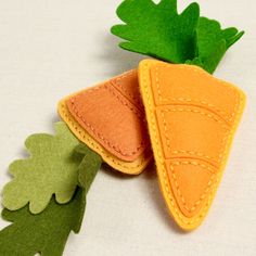 two felt carrots sitting next to each other on top of a white cloth surface