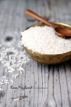 white rice in a bowl and wooden spoon on a table with scattered rice flakes