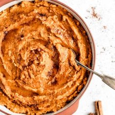 a bowl filled with cinnamon rolls on top of a white table next to two cinnamon sticks