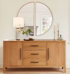 a wooden sideboard with a mirror and vase on it in front of a white wall